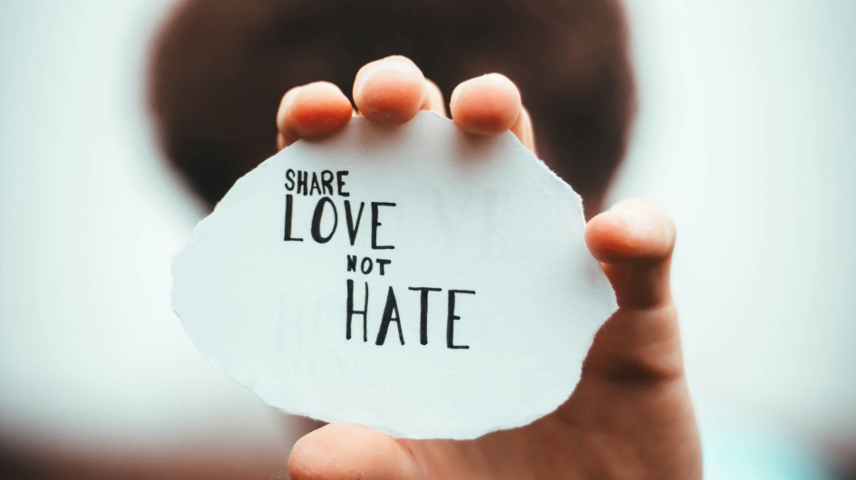 Person hält Share Love Not Hate Zettel in die Kamera