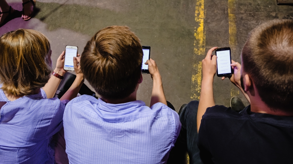 Drei Menschen sitzen und schauen auf ihr Handy (von hinten oben fotografiert)