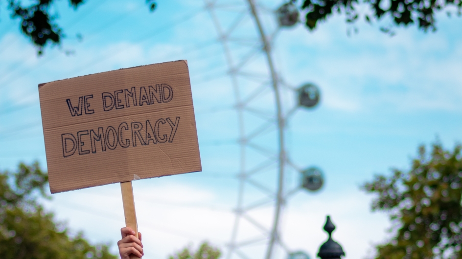 Schild mit Aufschrift "WE DEMAND DEMOCRACY"